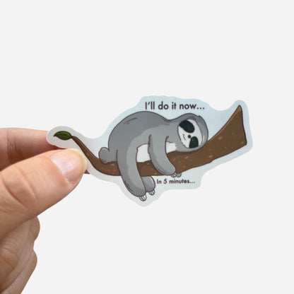 Sticker of a sloth on a branch with text, held by a hand against a white background