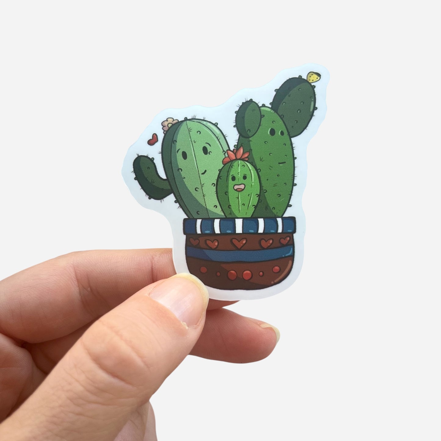 Hand holding a sticker with cartoon cacti design on a white background