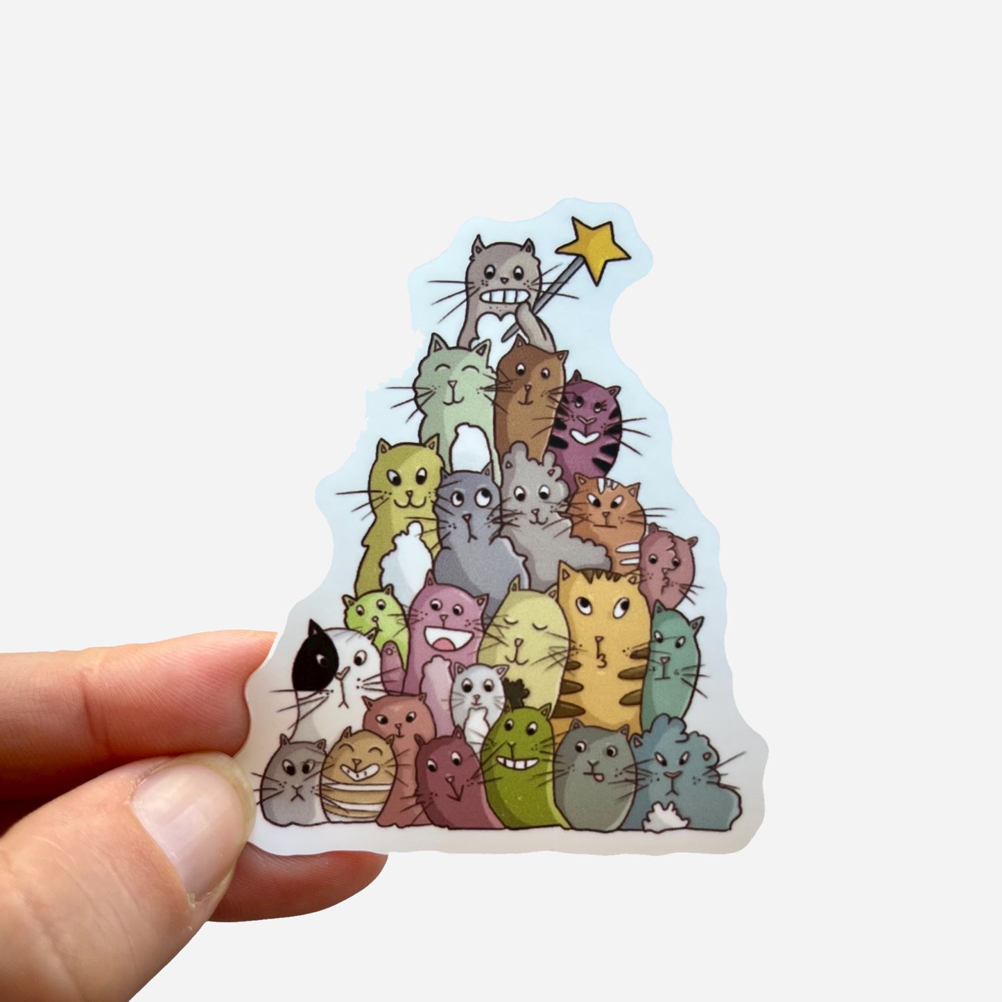 Hand holding a Catmas sticker showing a pyramid of colorful cats with a star on top, illustrated by Giulia Giampaolo.