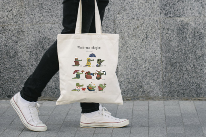 Person holding the Belgian Day tote bag with humorous crocodile illustrations, illustrated by Giulia Giampaolo.